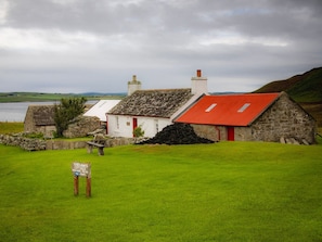 Une maison de campagne traditionnelle en pierre, avec un toit rouge, un mur en pierre et un champ verdoyant au premier plan.