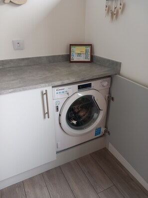 A compact laundry area with a Candy Smart washing machine, a small framed calendar, and a light switch on the wall.