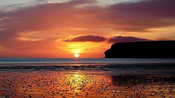 A sunset over a beach with a cliff in the background.
