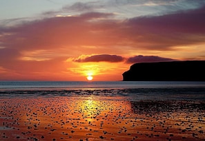 Un coucher de soleil sur une plage, avec une falaise en arrière-plan.