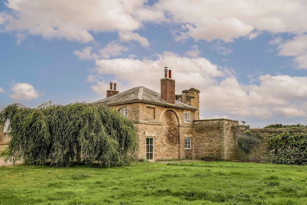 A historic stone building with a large arched doorway, a chimney, and a solar panel on the roof.