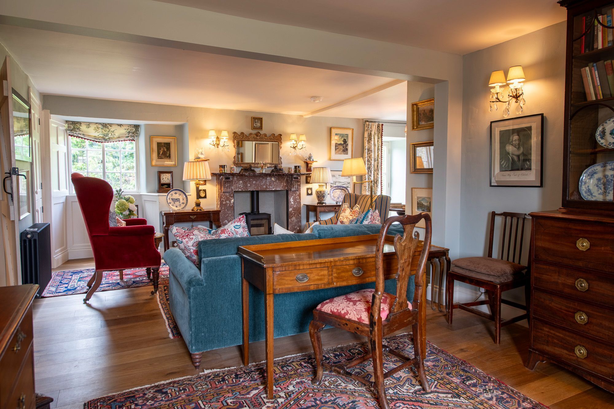 A traditional living room with a fireplace, a red armchair, a blue sofa, and a wooden coffee table.