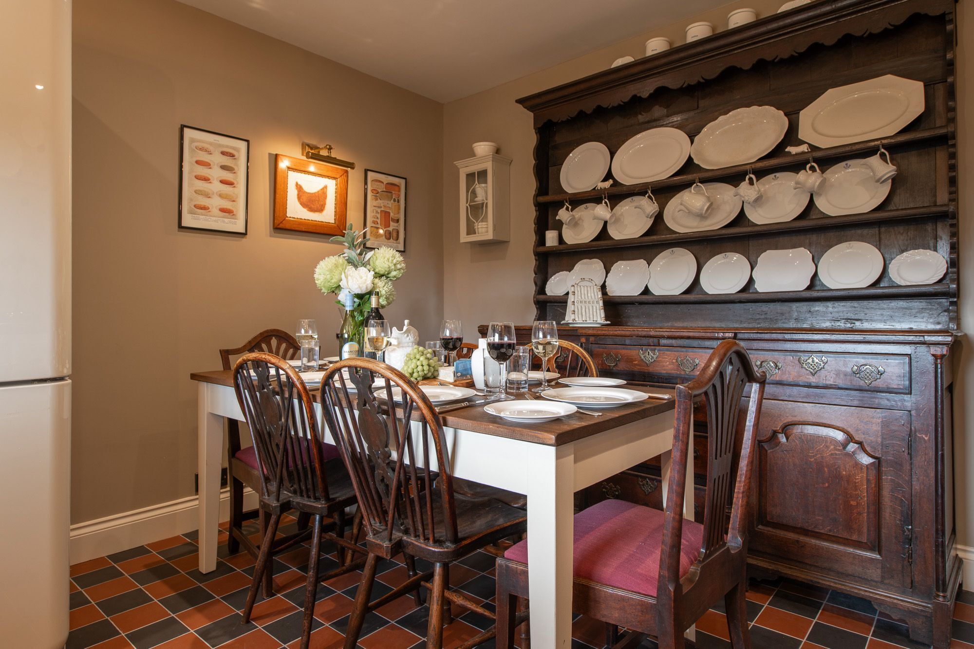 Un coin repas avec une table en bois, dressée pour quatre personnes, entourée de chaises, et un porte-assiettes fixé au mur au-dessus.