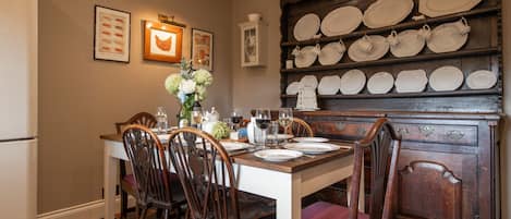 Un comedor con una mesa de madera dispuesta para cuatro personas, rodeada de sillas y un aparador con platos en la pared.