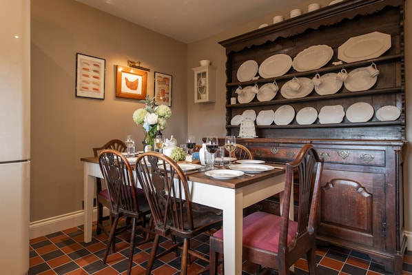 A dining area with a wooden table set for four, surrounded by chairs, and a wall-mounted plate rack above.