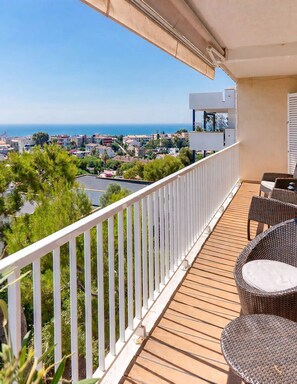 Ein Balkon mit Meer- und Stadtblick, möbliert mit Korbstühlen und einem Tisch.