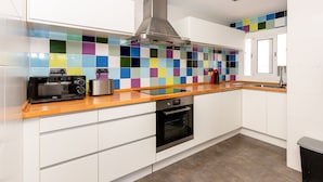 A modern kitchen with white cabinets, a stainless steel range hood, a colorful backsplash, and a wooden countertop. - Apartment Limoncello (Sant Pere de Ribes)