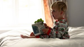 Un enfant est assis sur un lit, en train de lire un livre, avec une fenêtre en arrière-plan.
