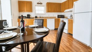 A modern kitchen with wooden cabinets, a dining table set for four, and a refrigerator. - LUX Mins to St George St - Anastasia Beach - Flagler Hospital - Sunrise (St. Augustine)