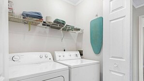 A laundry room with two white washing machines, a shelf with folded clothes, and a teal towel rack. - LUX Mins to St George St - Anastasia Beach - Flagler Hospital - Sunrise (St. Augustine)