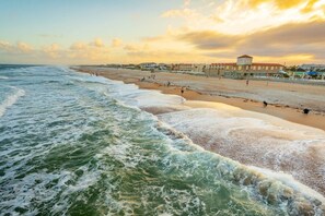 Ein Strand mit Wellen, einer Promenade und Gebäuden im Hintergrund.