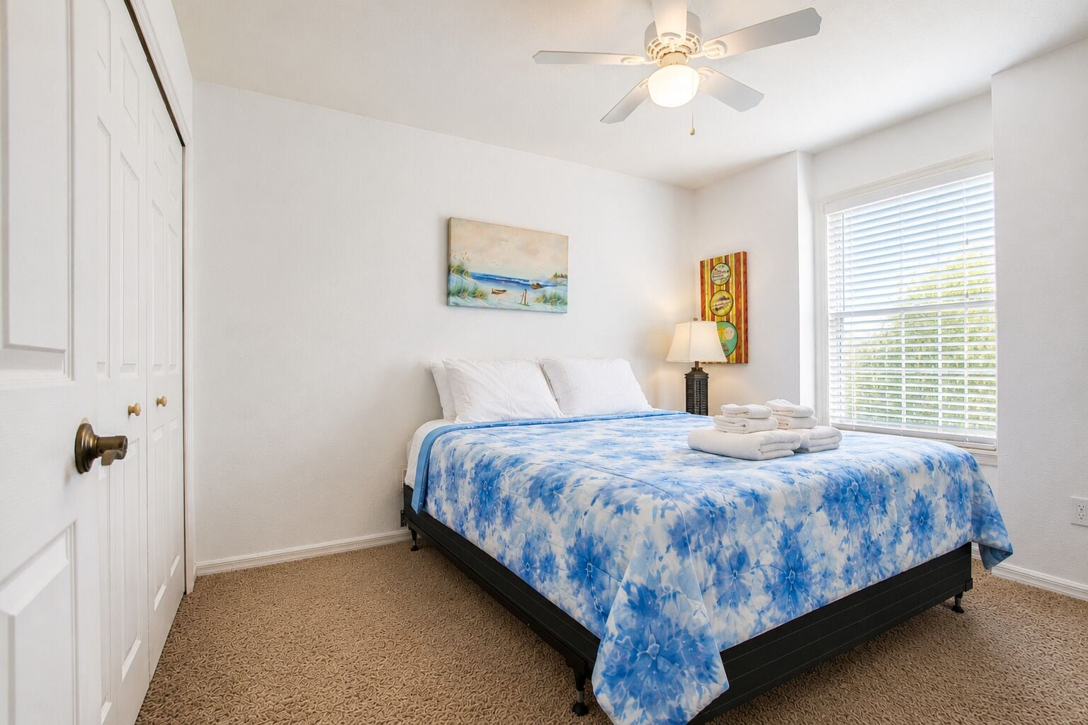 A bedroom with a bed, a ceiling fan, a window with blinds, and a door.