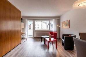 A modern living room with a wooden wardrobe, a red table, a black sofa, and a window with a view of buildings. - Victoria B Studio - InspiringPlaces  (Zermatt)