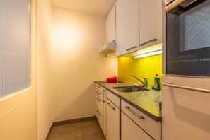 Cocina compacta con armarios blancos, encimera de granito, un lavamanos y una ventana con persianas.