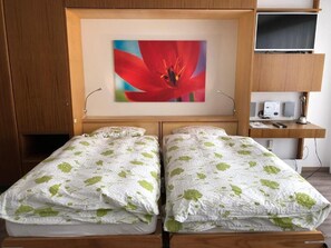 A room with two beds, a desk, a television, and a wall-mounted speaker. - Victoria B Studio - InspiringPlaces  (Zermatt)