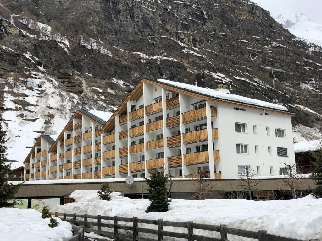 Een meerlaags hotel met balkons, gelegen tegen een bergachtige achtergrond.