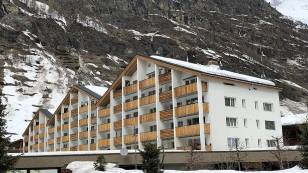 A multi-story hotel with balconies, set against a mountainous backdrop. - Victoria B Studio - InspiringPlaces  (Zermatt)