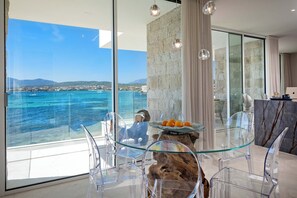 Un comedor moderno con una mesa de vidrio, sillas transparentes y vistas al mar.