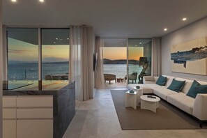 Salón moderno con un amplio ventanal que ofrece vistas al mar y al atardecer.