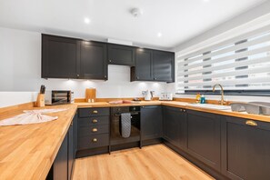 Eine moderne Küche mit dunklen Schränken, Holzarbeitsplatten, einem eingebauten Backofen und einem Fenster mit Jalousien.