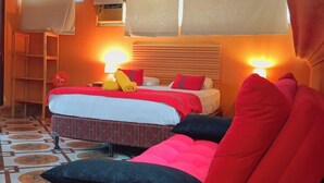 A hotel room with two beds, a red chair, a standing fan, and a window with curtains. - La Casa Colorada (San Benito)