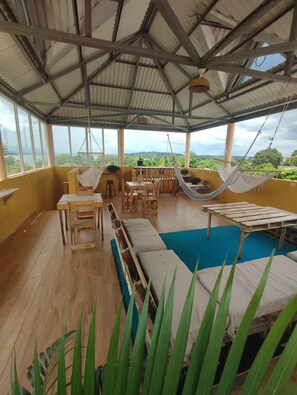 Un espacio al aire libre cubierto con piscina, mobiliario de madera y una hamaca.