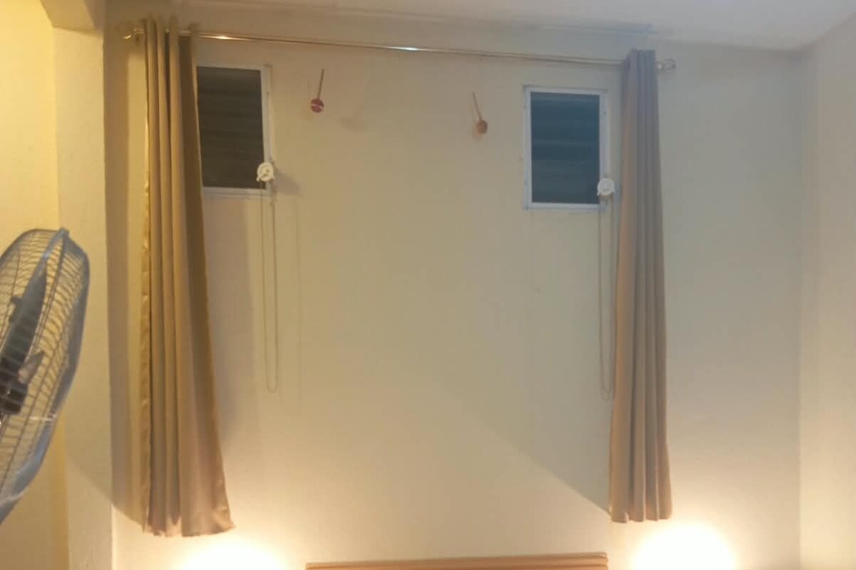 Una habitación de hotel con una cama, dos lámparas de noche, una silla, un ventilador y cortinas.