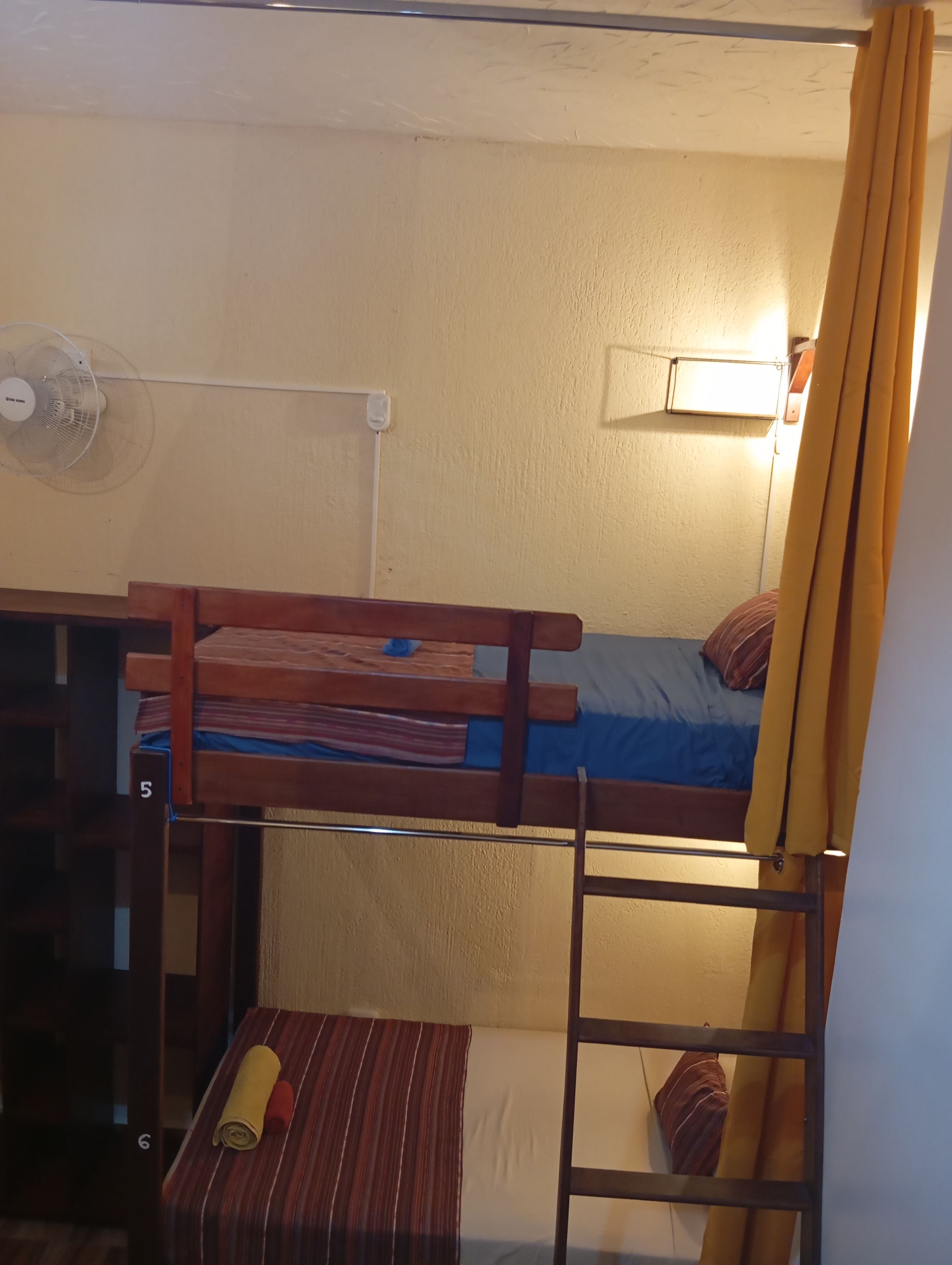 Een stapelbed met een bureau en stoel, een tafeltje met een opgerolde mat, en een ladder.