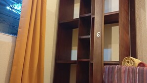 A room with a wooden bookshelf, a window with curtains, and a bed with a striped blanket.