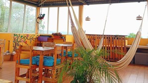 A spacious indoor area with wooden furniture, a hammock, and large windows allowing natural light.