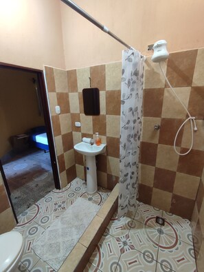 Un baño con inodoro, lavabo, ducha y baldosas de suelo estampadas.