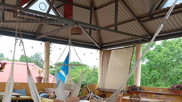 A covered outdoor seating area with wooden tables and chairs, hammocks, and a view of greenery. - La Casa Colorada (San Benito)