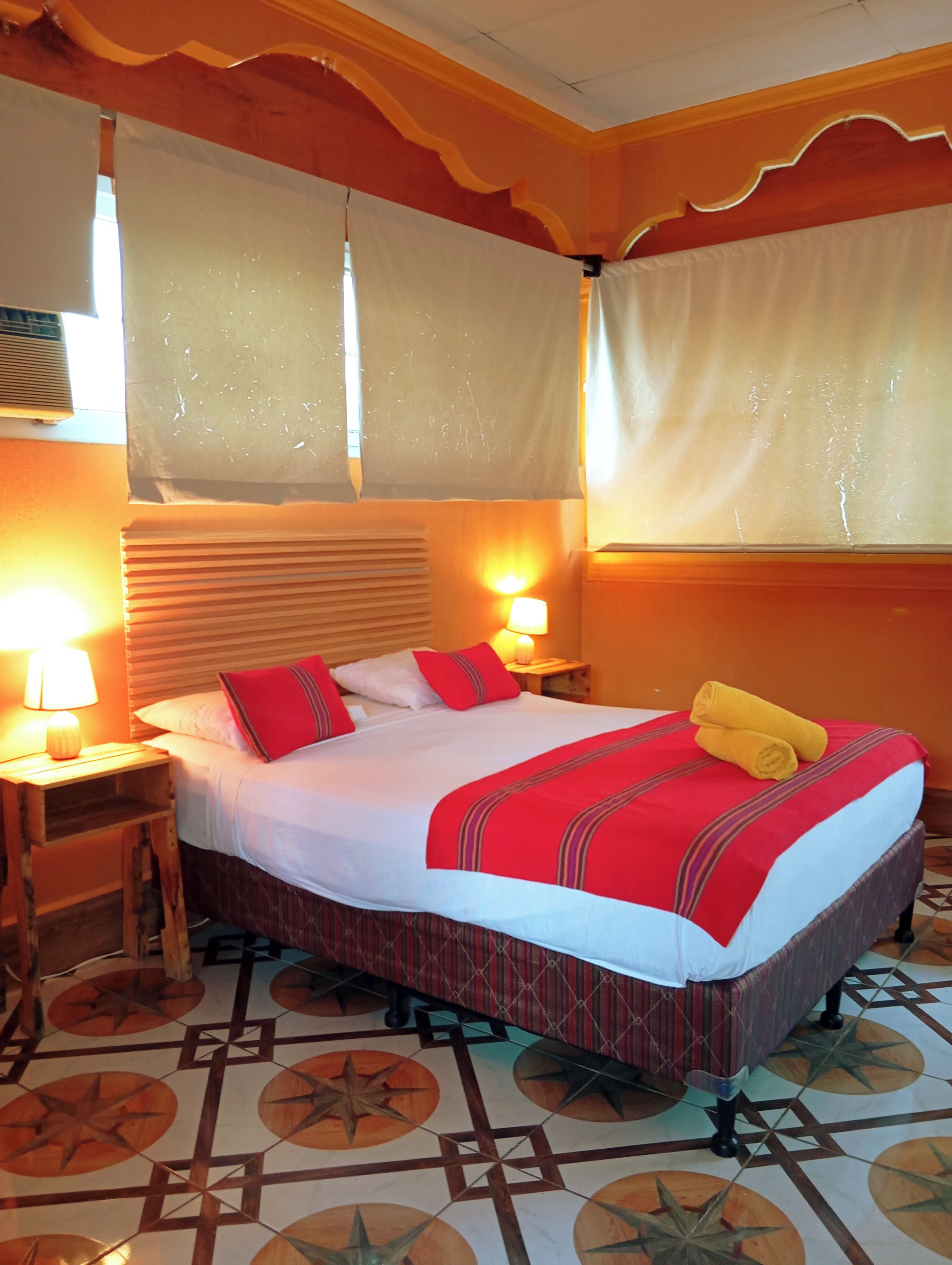 Habitación de hotel con cama, dos lámparas de noche, una mesita de noche y piso estampado.