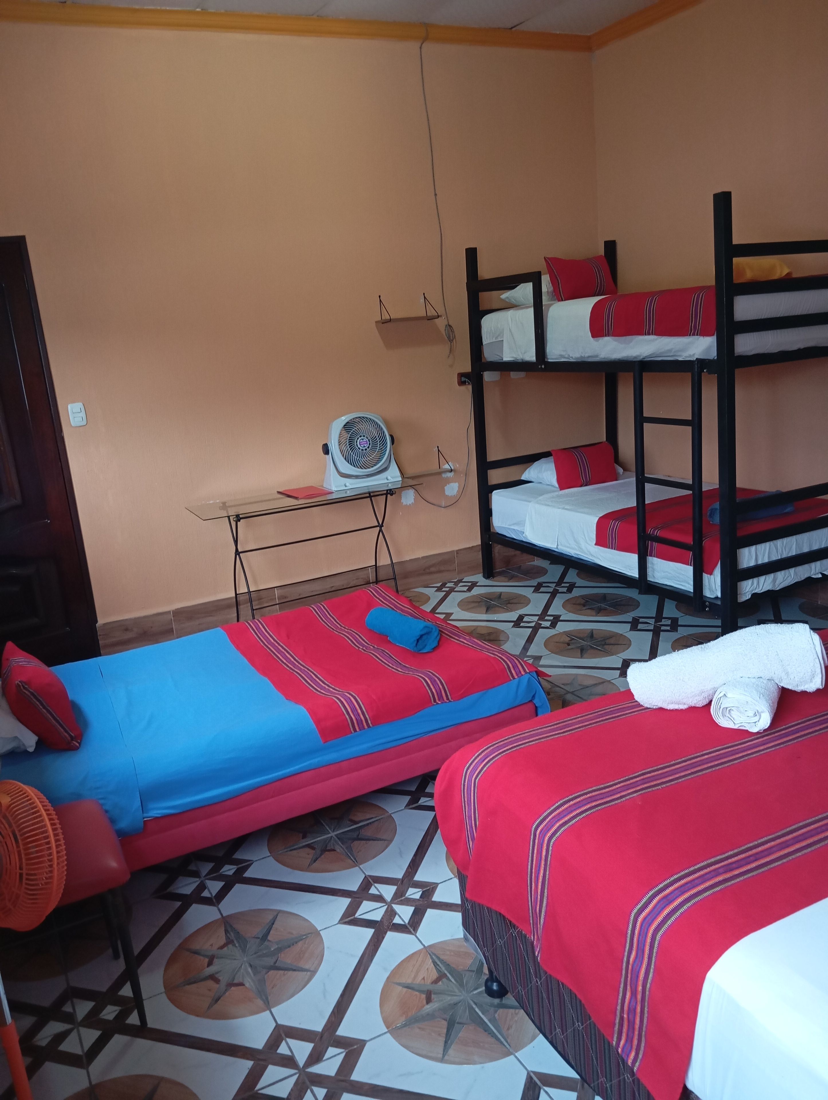 Um dormitório com beliches, um ventilador e uma mesa com cadeira.