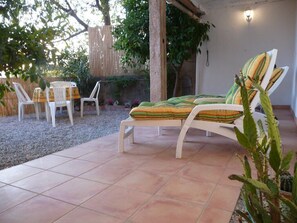 Un espace patio avec un fauteuil de jardin blanc et une petite table, entouré d’une clôture en bois et de verdure.