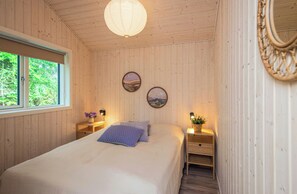 A bedroom with a bed, two bedside tables with lamps, a window, and two wall-mounted paintings.