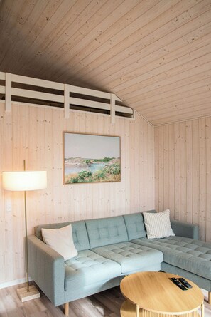 A room with a light blue sectional sofa, a round wooden coffee table, and a painting of a landscape on the wall.