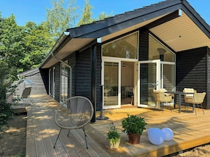 Et moderne træhus med en terrasse, en glasdør ind til et opholdsrum og udendørs møbler.