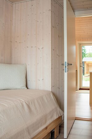 A bedroom with a wooden wall, a bed with a patterned bedspread, and a door leading to an outdoor area.