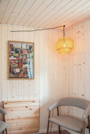 A room with wooden panel walls, a framed cityscape artwork, a woven light fixture, and two chairs.