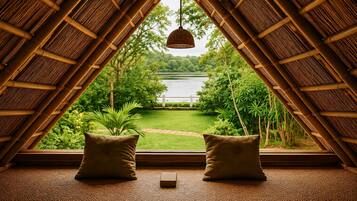 A room with a view of a lake, a hanging light fixture, and two pillows on the floor.