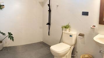 A bathroom with a toilet, a shower, a sink, and a potted plant.