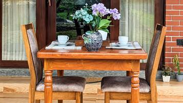 Une table de salle à manger en bois, accompagnée de deux chaises, d’un vase avec des fleurs et d’une tasse avec sa soucoupe.