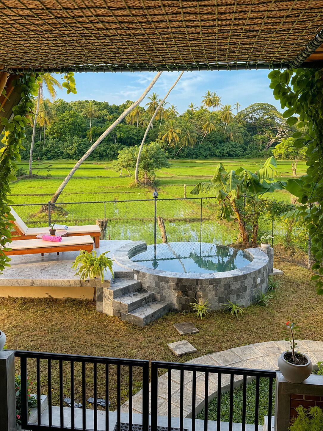 Un espace piscine privé doté d’une terrasse en pierre, de chaises longues et offrant une vue sur un paysage verdoyant luxuriant, parsemé de palmiers.
