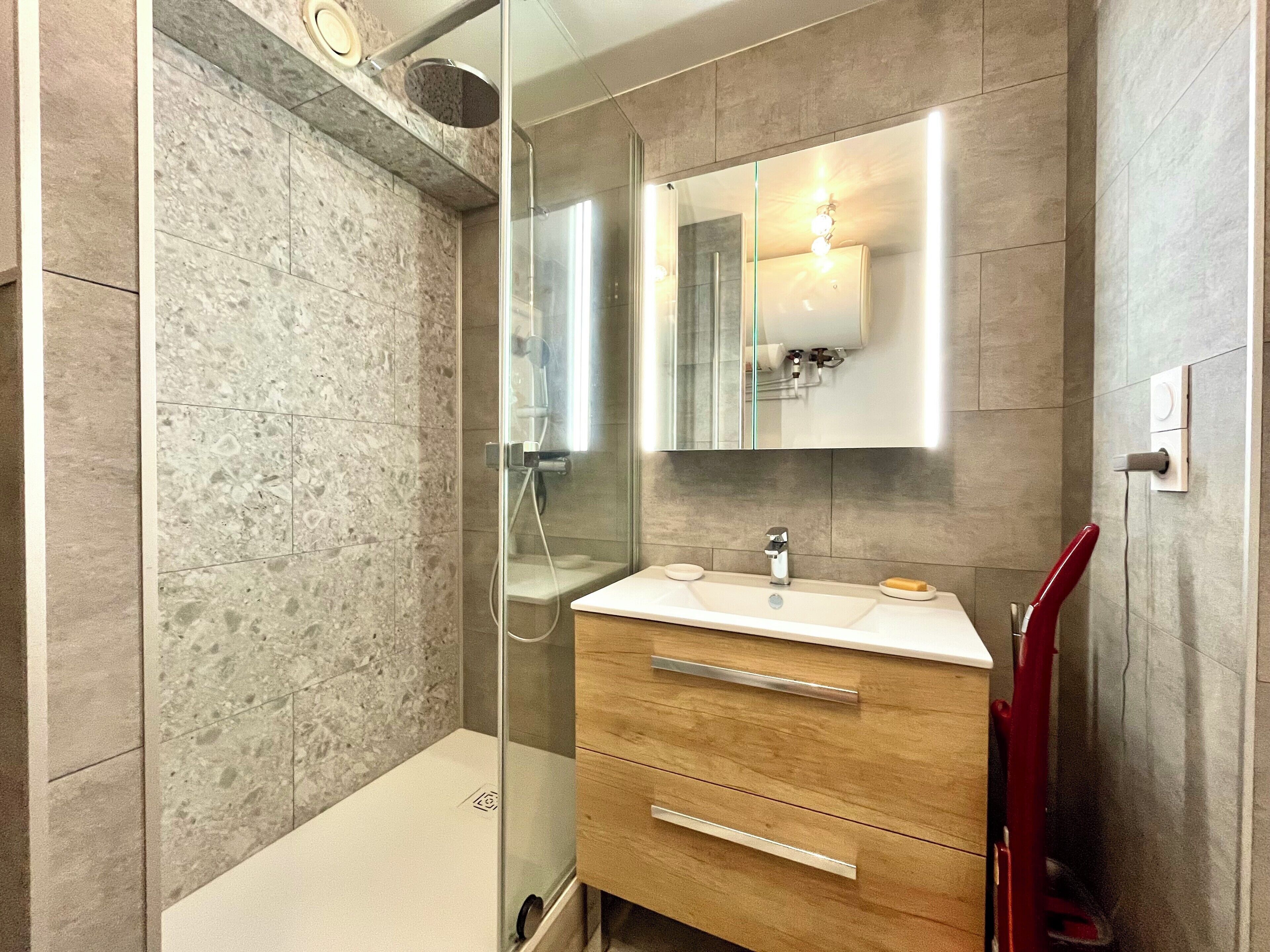 Une salle de bain moderne avec une douche à parois de verre, un meuble-lavabo en bois avec un miroir et un porte-serviettes rouge.