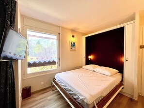 A bedroom with a bed, a window, a wall-mounted TV, and a door. - Studio in the heart of Combloux near the lake (Combloux)