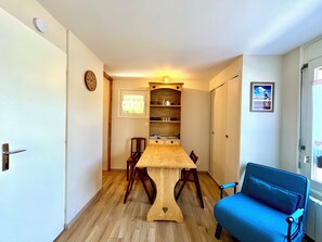 A dining area with a wooden table and chairs, a bookshelf, and a blue sofa. - Studio in the heart of Combloux near the lake (Combloux)