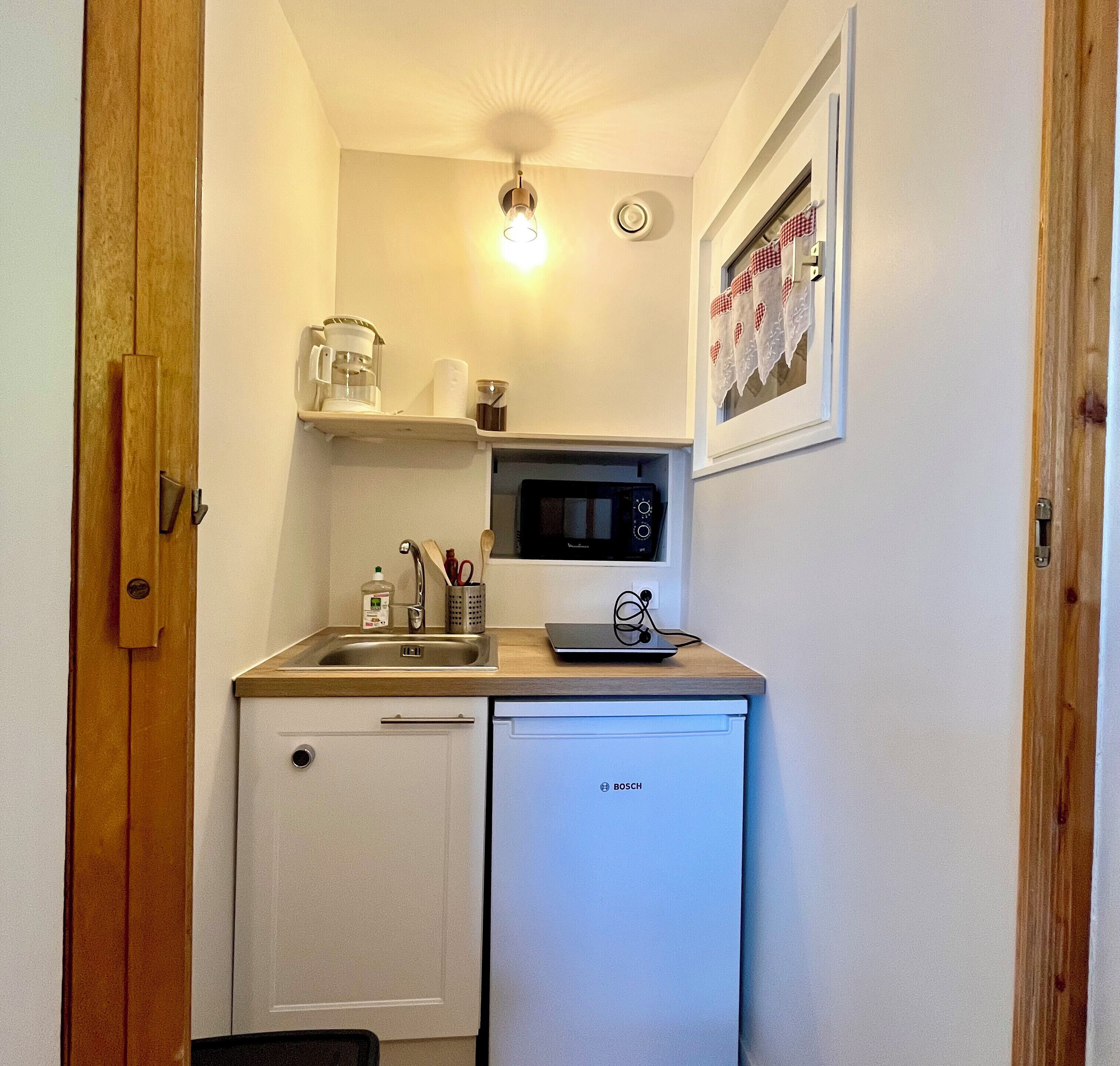 Una kitchenette compacta equipada con microondas, cafetera y lavavajillas Bosch.