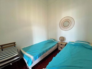 Ein Schlafzimmer mit zwei Einzelbetten, einer hölzernen Bank, einem Wandspiegel und einem kleinen dekorativen Gegenstand auf dem Nachttisch.