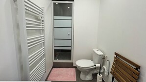 Uma casa de banho compacta com sanita, chuveiro e armário.
